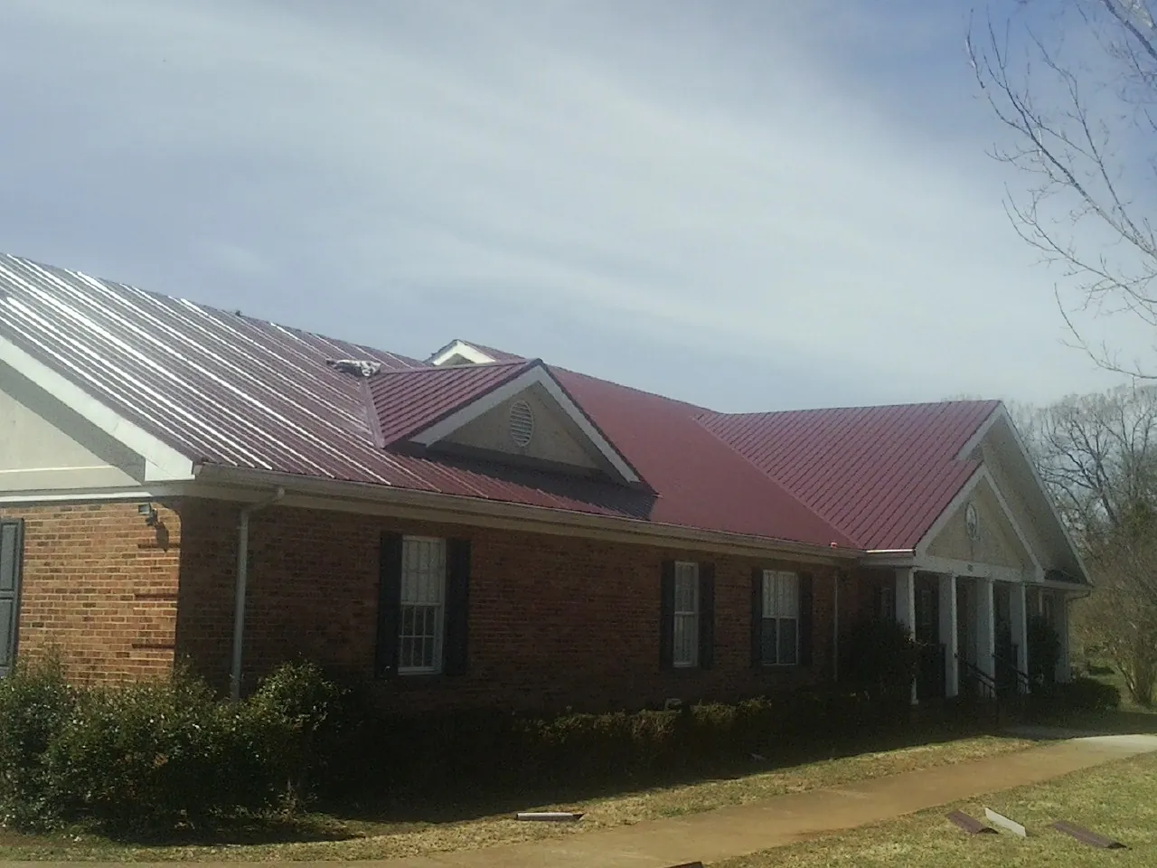 Red metal roof with gabled entries on a long brick building, from a Hail Damage Roof Repair job in Luther