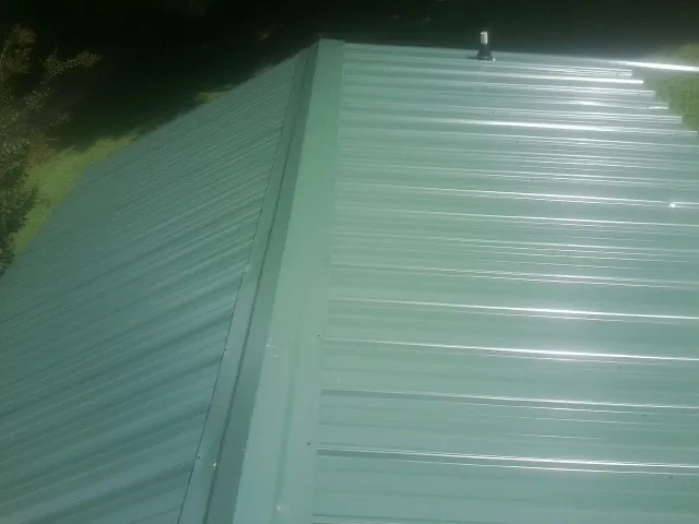 New green metal panels meeting at the ridge of a roof — Flat Roof Repair work by our crew in Luther